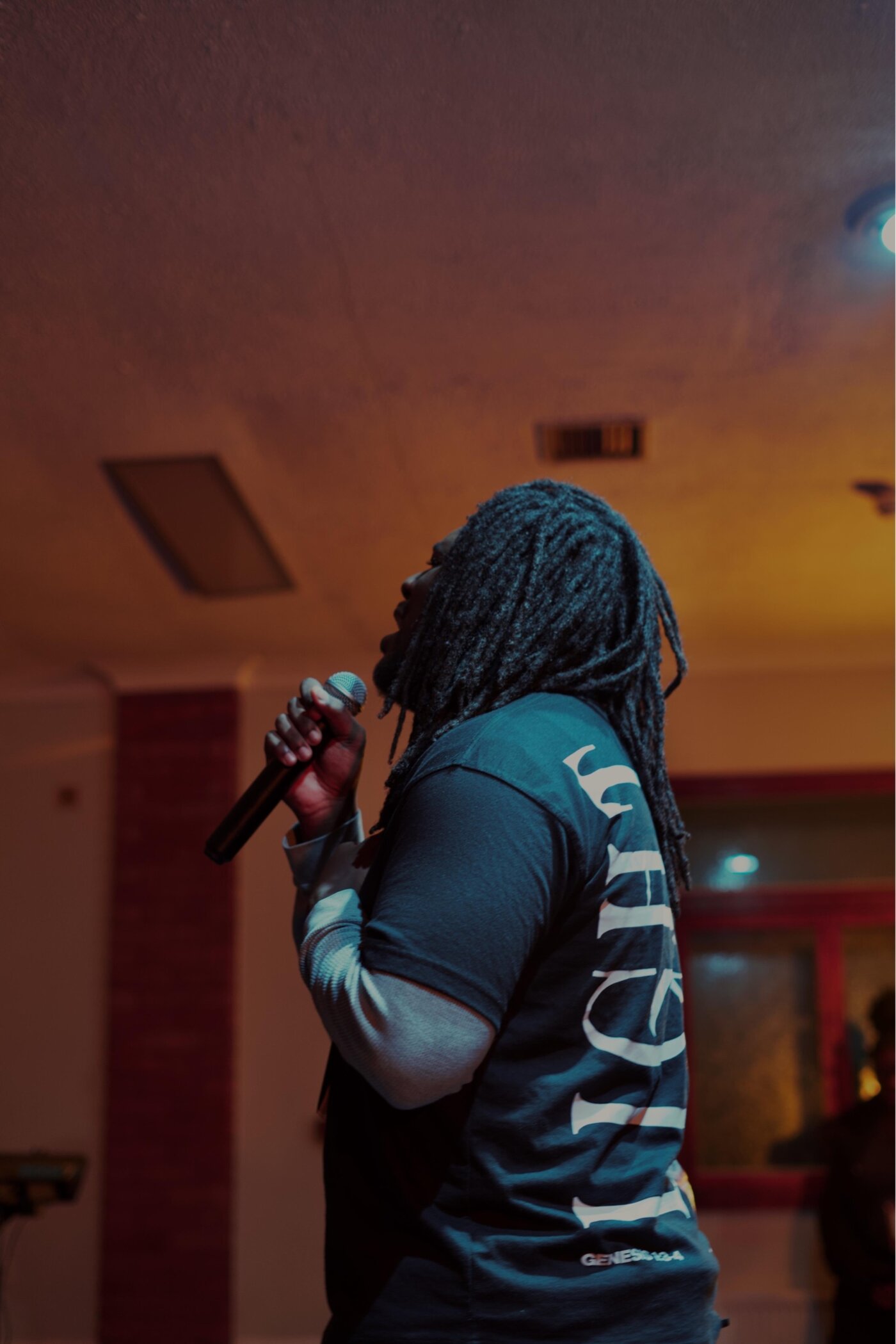 A worship leader sings into a microphone, backlit on stage.